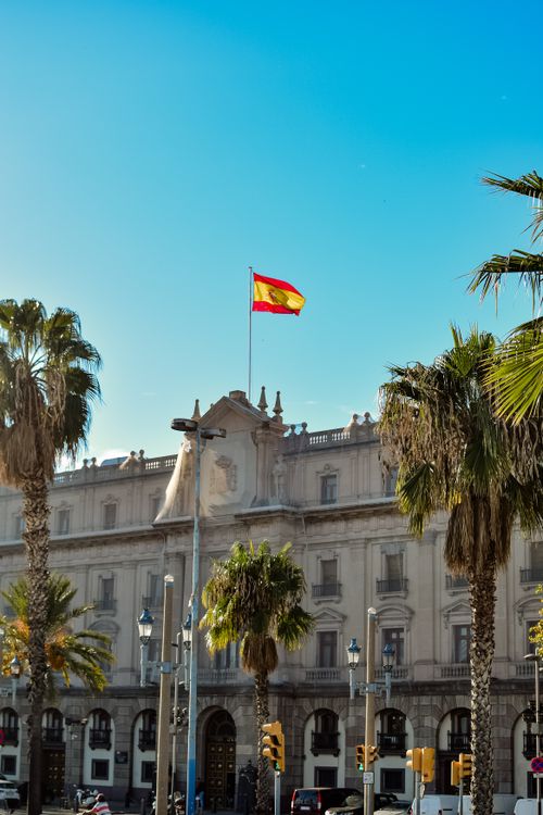 Grand palace facade with Spanish flag and palm trees in Barcelona
