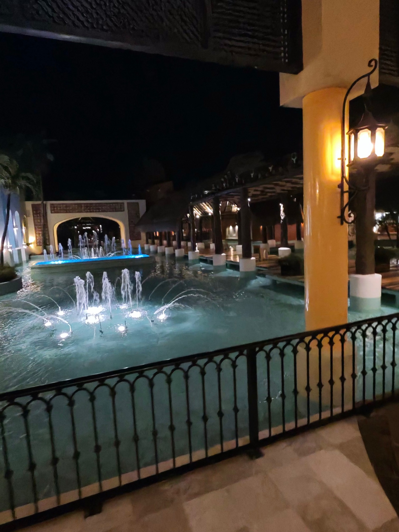 Lit blue fountains under wooden pergola at night