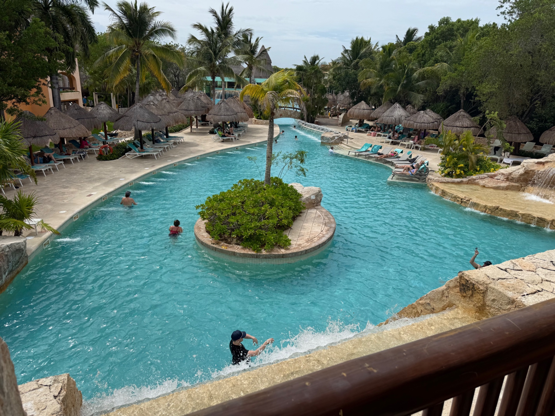 Winding turquoise pool with palm-covered island and thatched palapas at Iberostar Paraiso Maya Suites